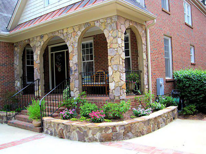 Photo of stone raised beds with flowers and mulch on front of a house
