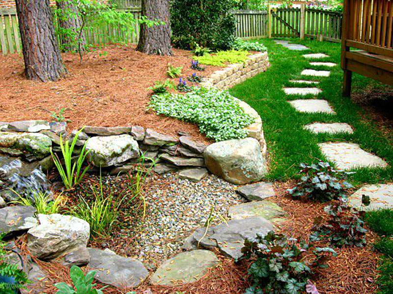 Photo of a hardscaped rock waterfall with plants and slate pathway